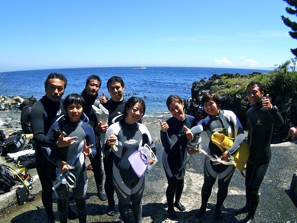 城ヶ崎海岸の海をバックに記念撮影する体験ダイビング参加者